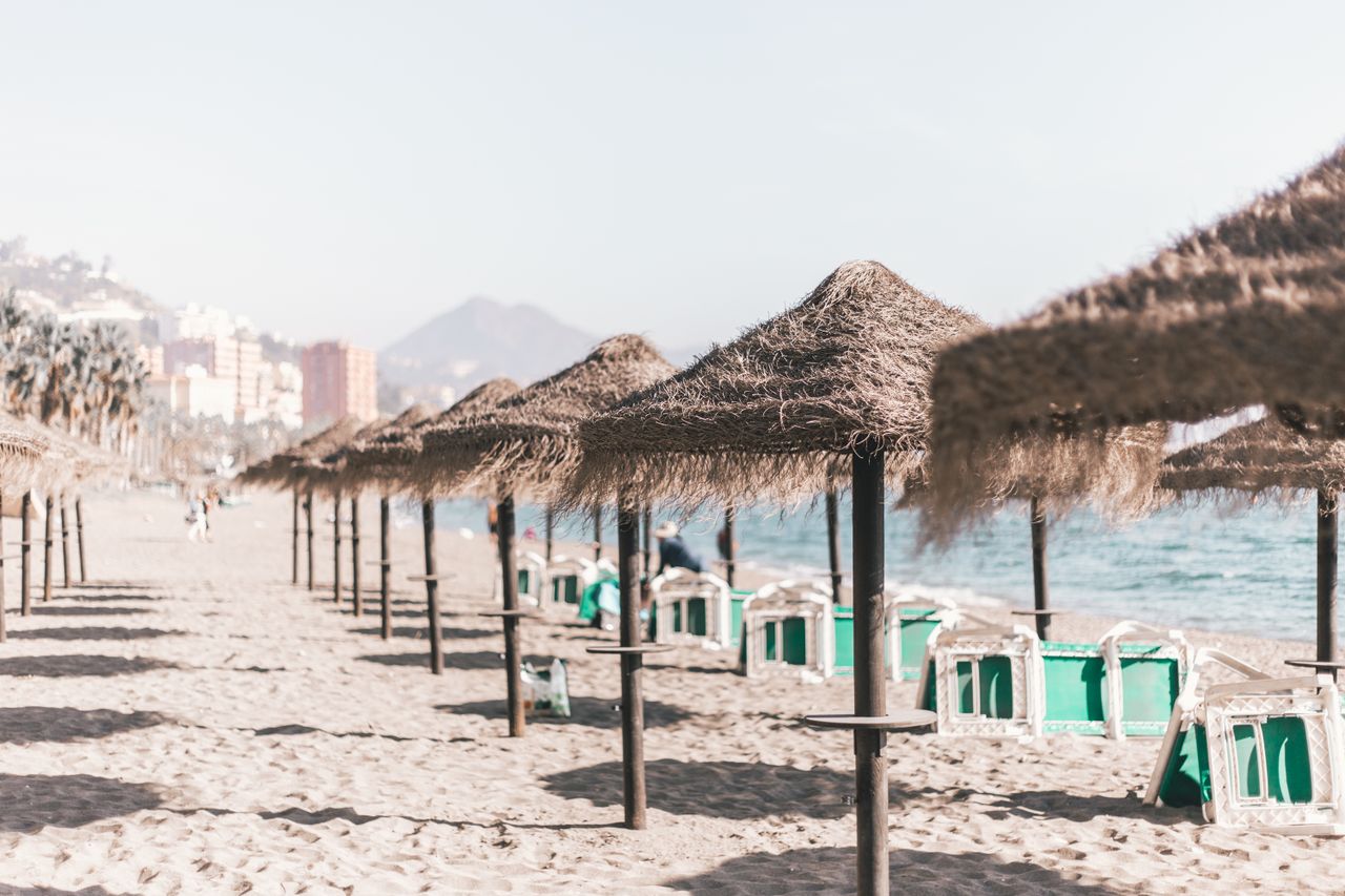 services-03 A serene sandy beach with straw umbrellas and clear skies, perfect for a summer vacation in Malaga, Spain.