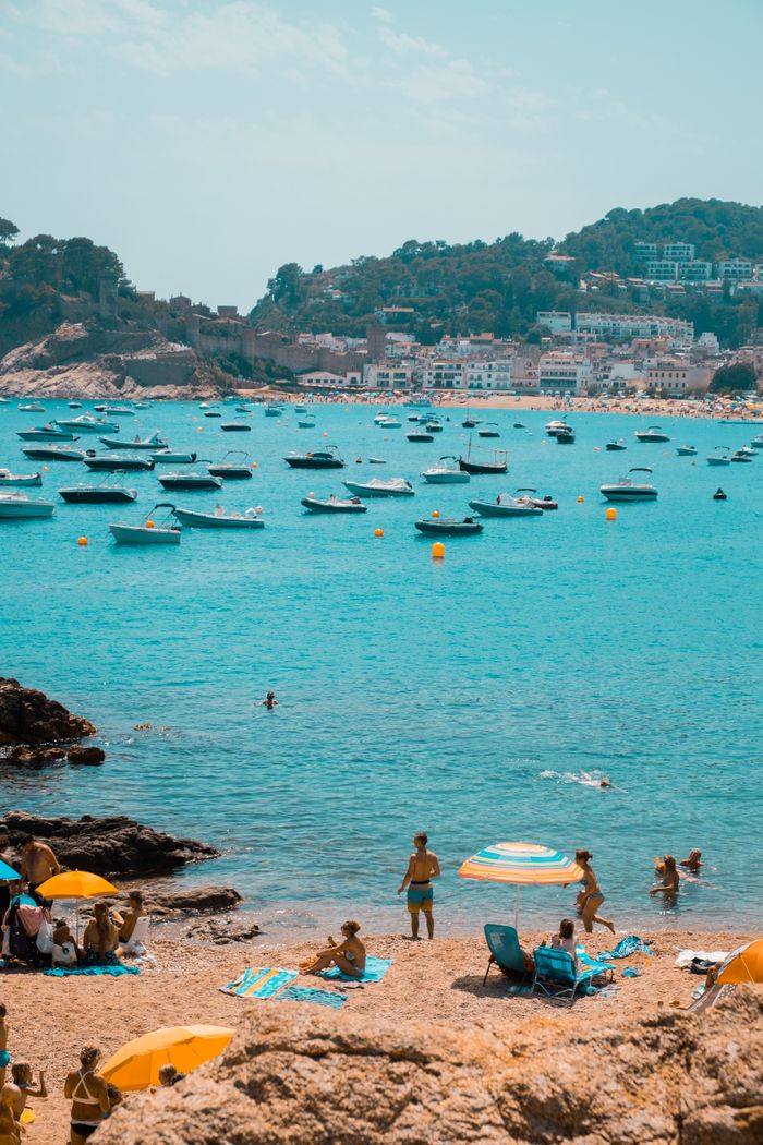 Relaxing summer beach scene in Tossa de Mar, Spain with turquoise waters and boats.